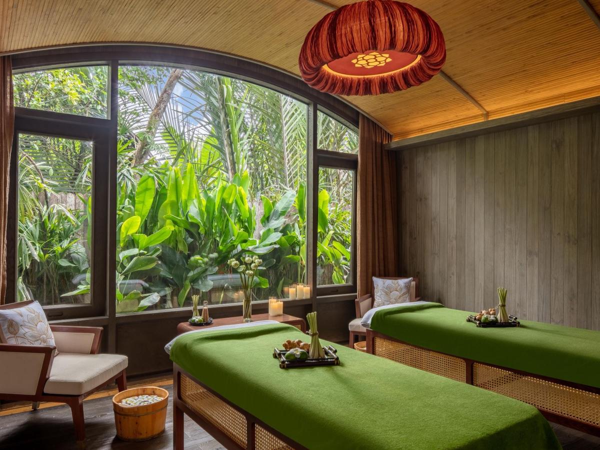 Twin treatment room with green-draped massage beds under a red lantern and arched windows onto foliage