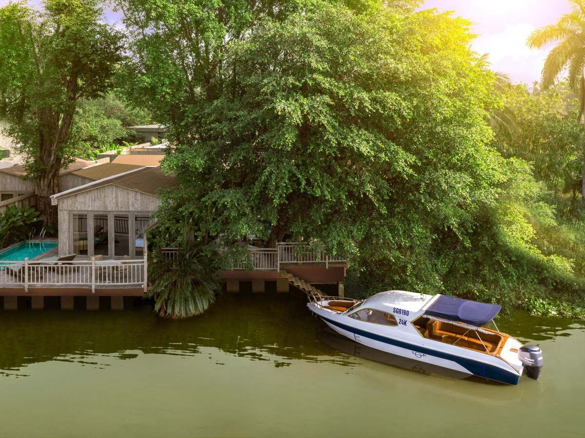 White speedboat moored at a timber jetty in front of a riverside villa with a small pool