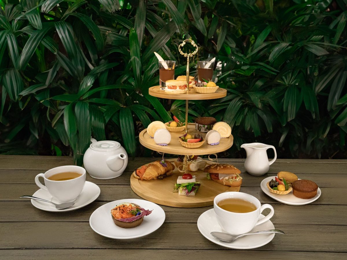 Afternoon tea stand with pastries and cups of tea on a table in a green garden