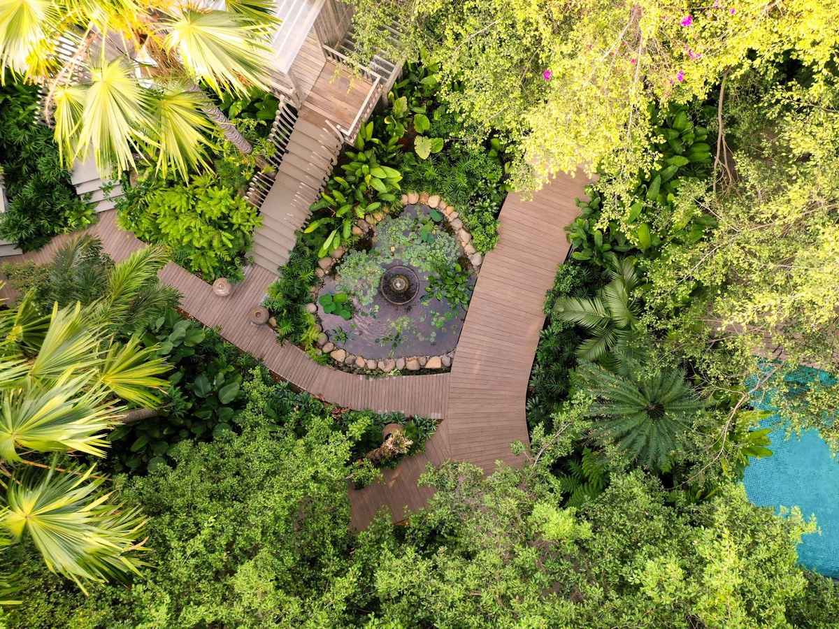 Aerial view of winding garden paths and a round courtyard hidden in thick tropical trees