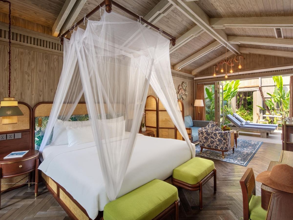 Canopy bed with a white net under a pitched timber ceiling, glass doors open to a private pool