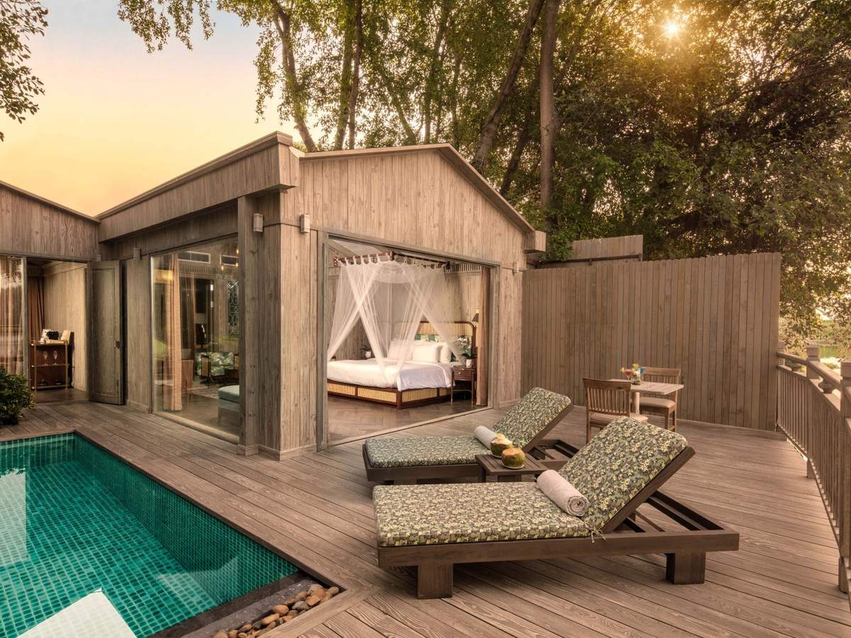 Turquoise private pool and loungers beside a timber villa with its bedroom open to the deck at dusk