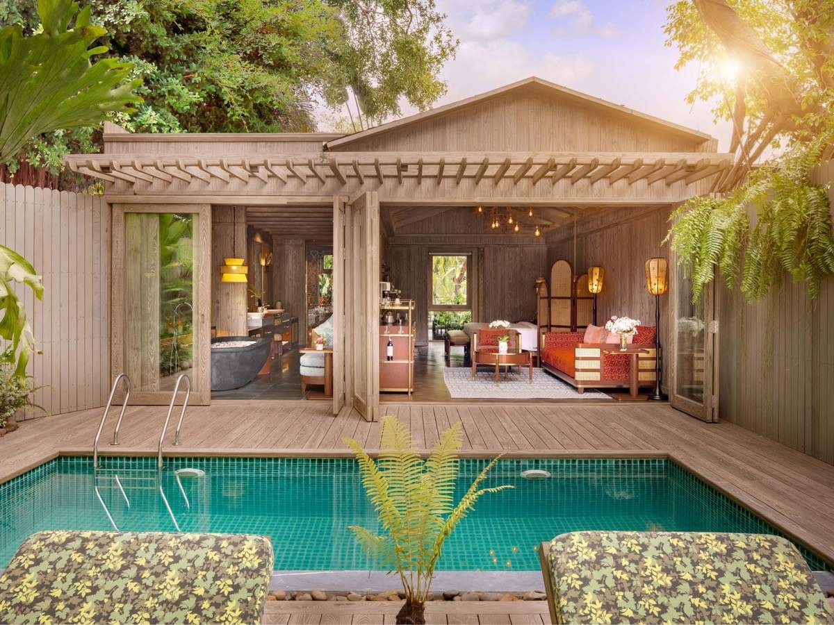 Private pool in front of a grey timber villa with a gabled roof and an open living room, framed by palms