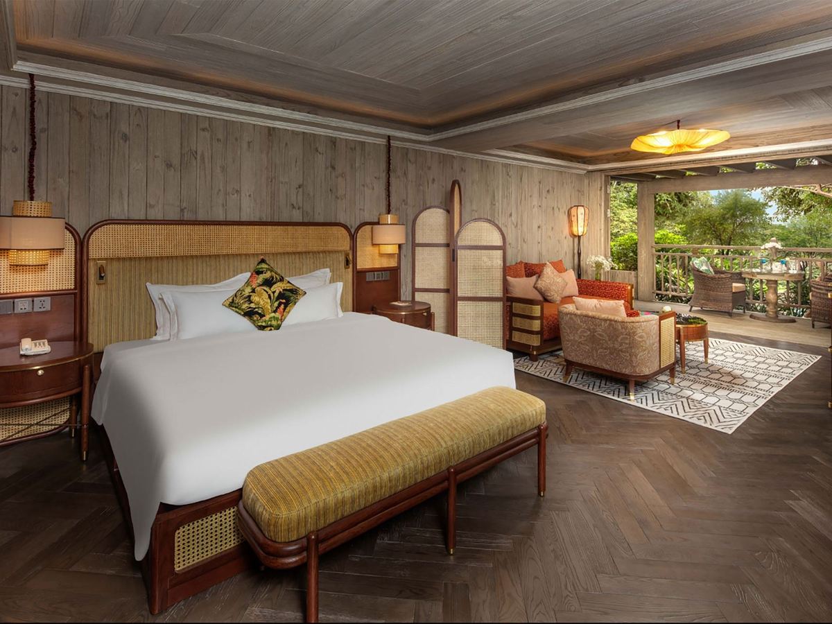 Suite bedroom with a rattan headboard, timber-clad walls and open doors to a leafy terrace