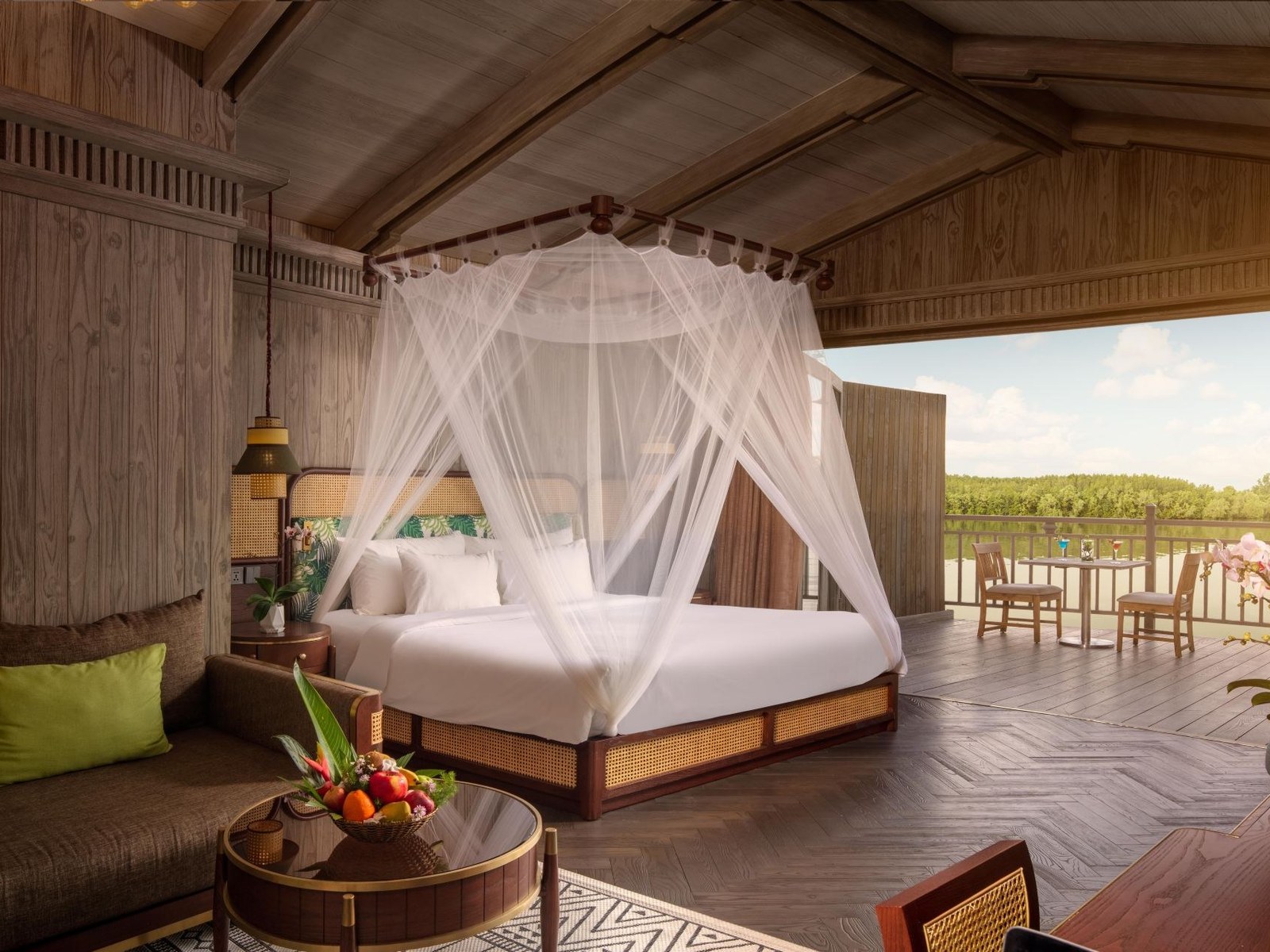 Canopy bed with a white mosquito net in an open timber room looking across a terrace to the river